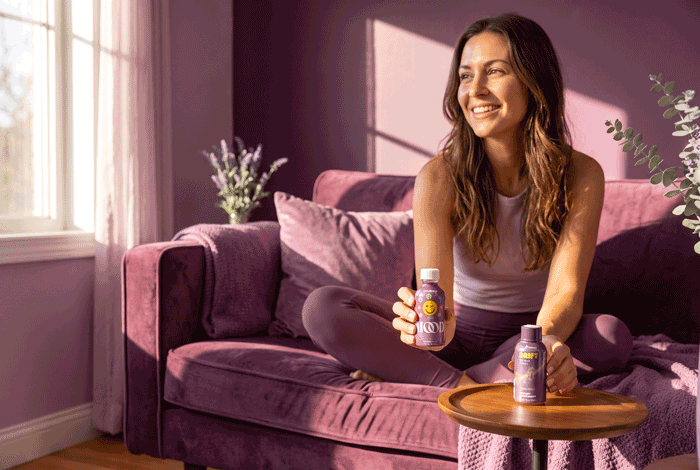 a woman sitting on a couch holding two bottles of vitamins